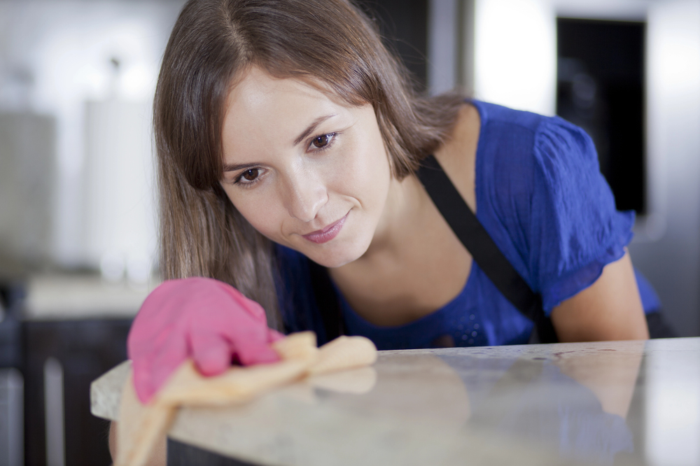 Happy young housewife in pink gloves cleaning a glass table in the kitchen
